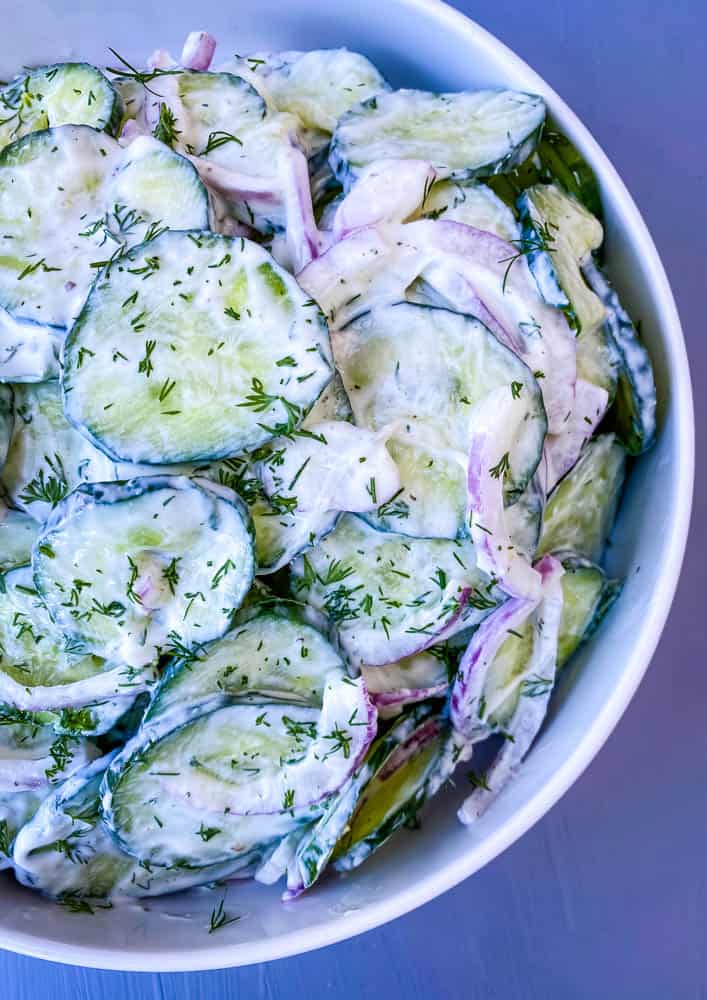 creamy cucumber salad with red onions in a white bowl