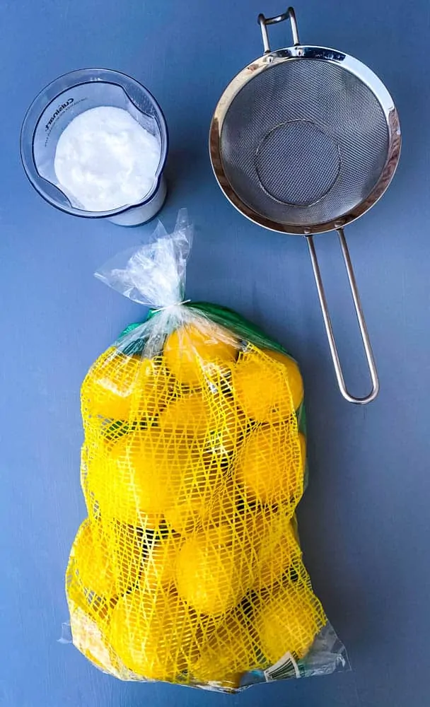 fresh lemons, sweetener, and a strainer on a flat surface