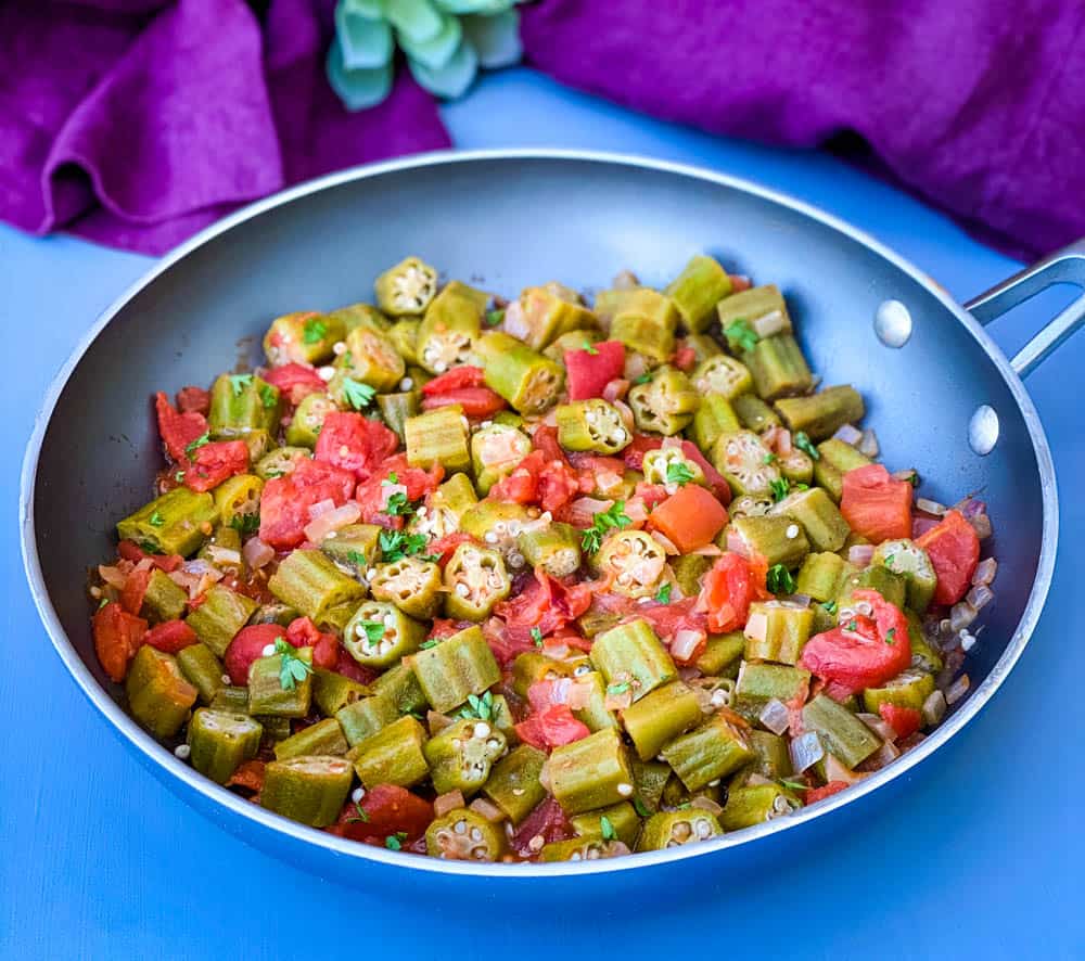 okra and tomatoes in a skillet with a purple napkin
