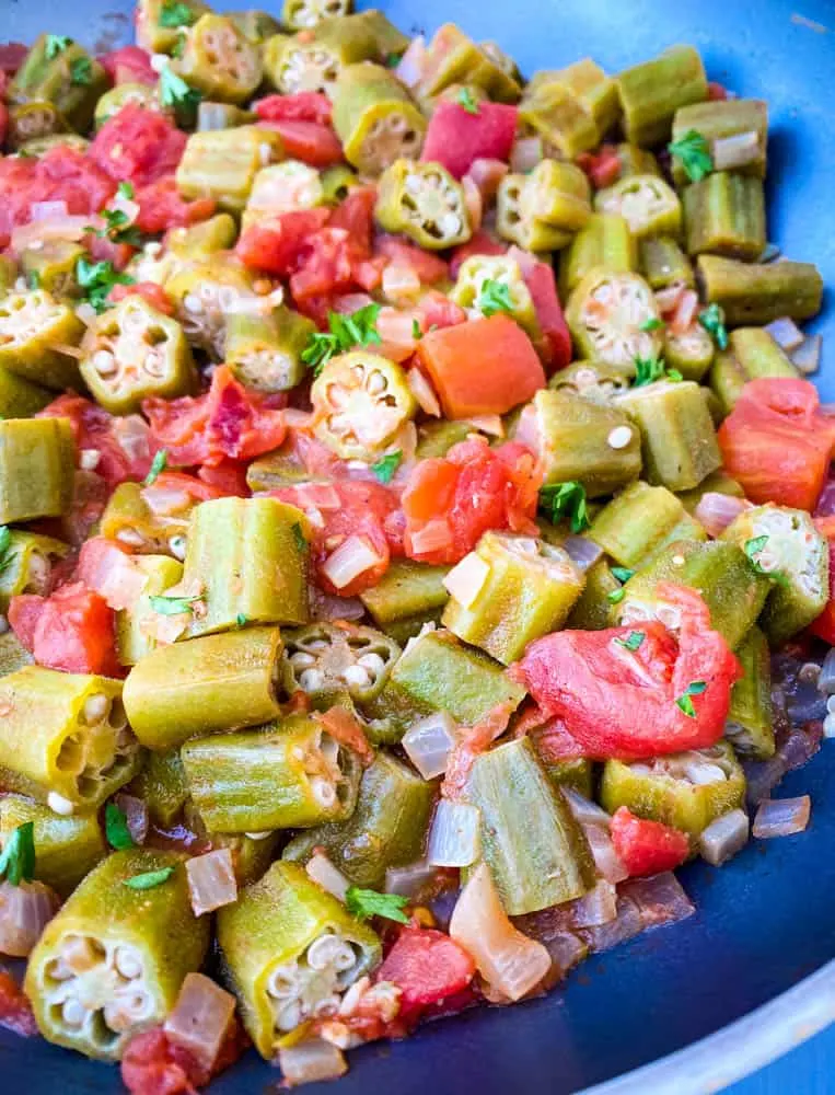close up photo of okra and tomatoes in a pan