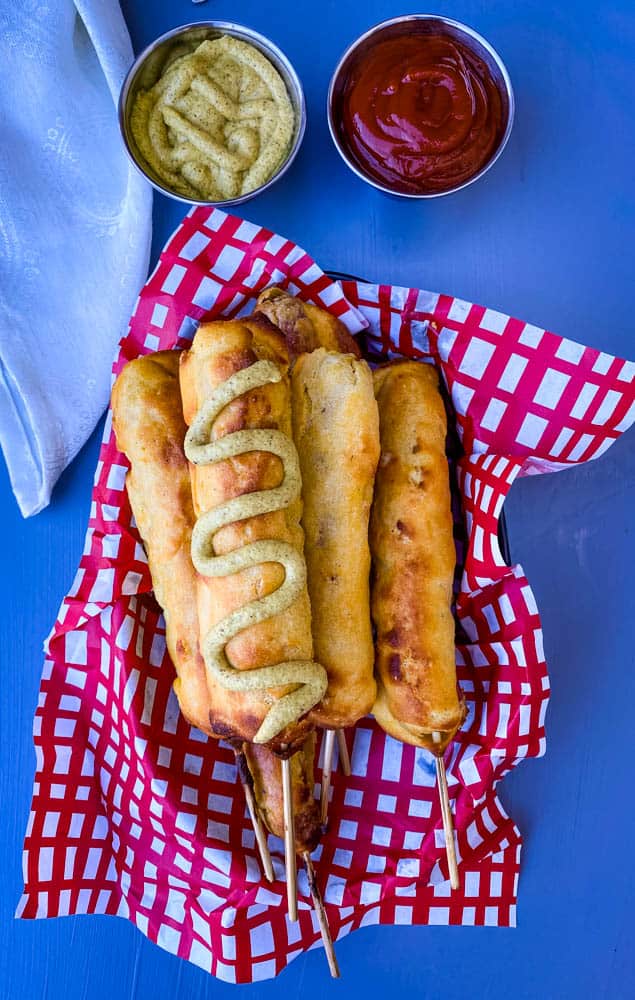air fryer corn dogs with mustard in a basket with a red and white napkin