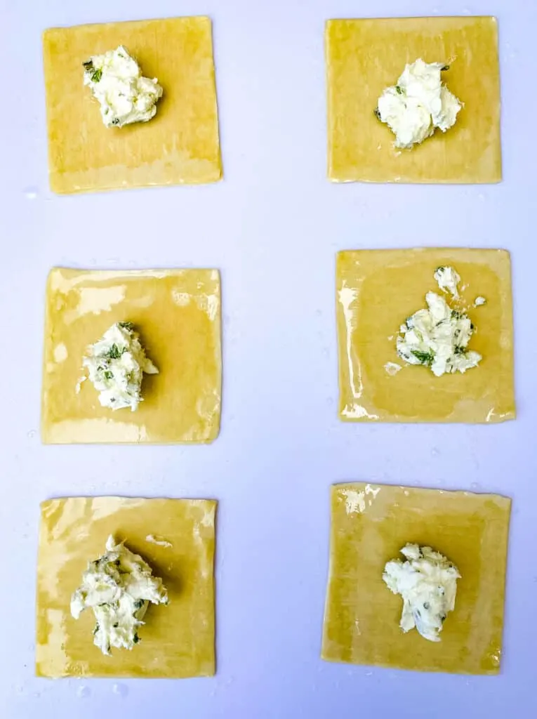 wonton wrappers with cream cheese filling on a white cutting board