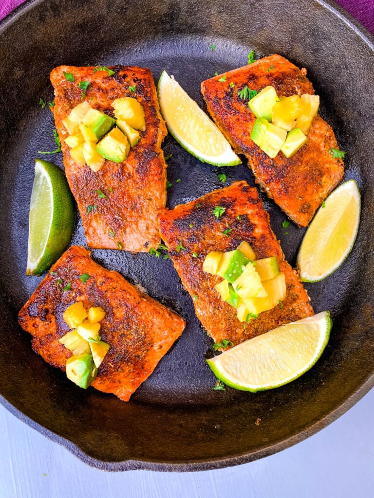 blackened salmon in a cast iron skillet topped with pineapple and avocado