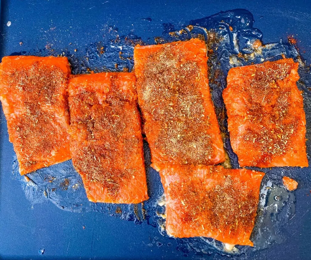 raw and seasoned salmon on a cutting board