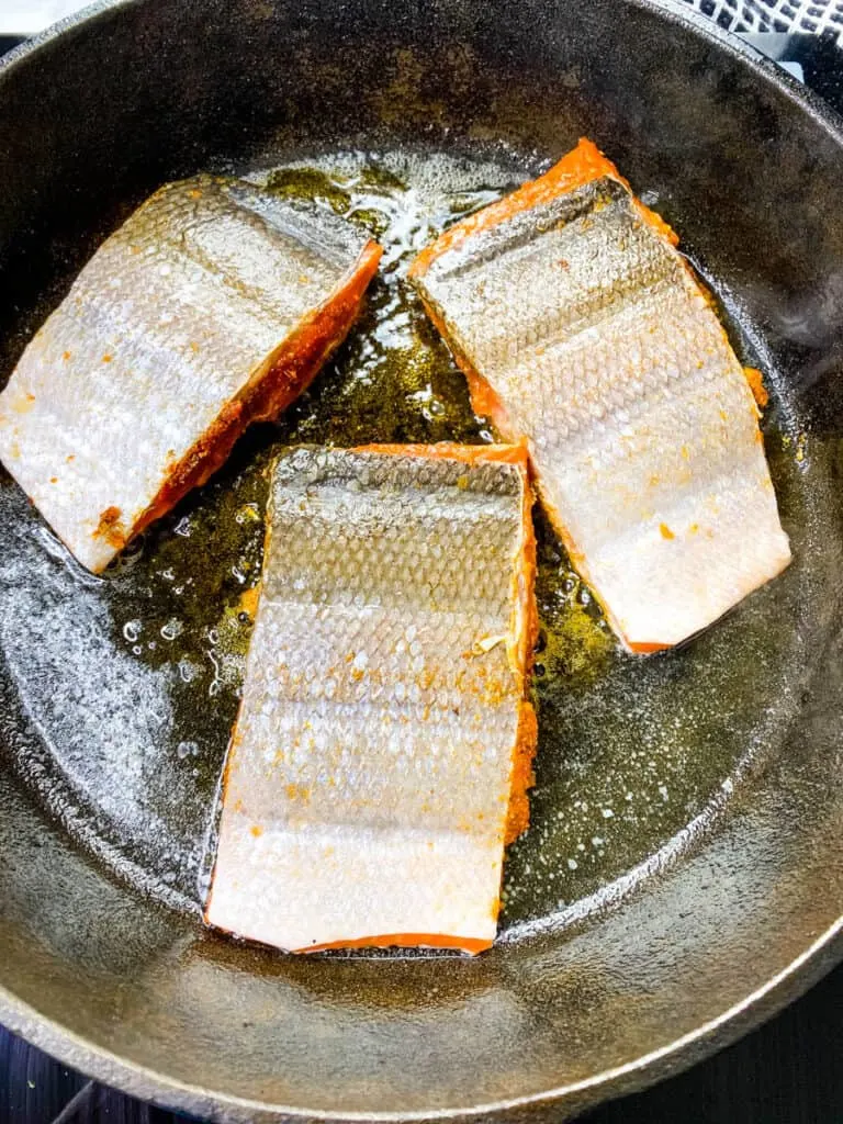 blackened salmon with the skin on cooking in a cast iron skillet