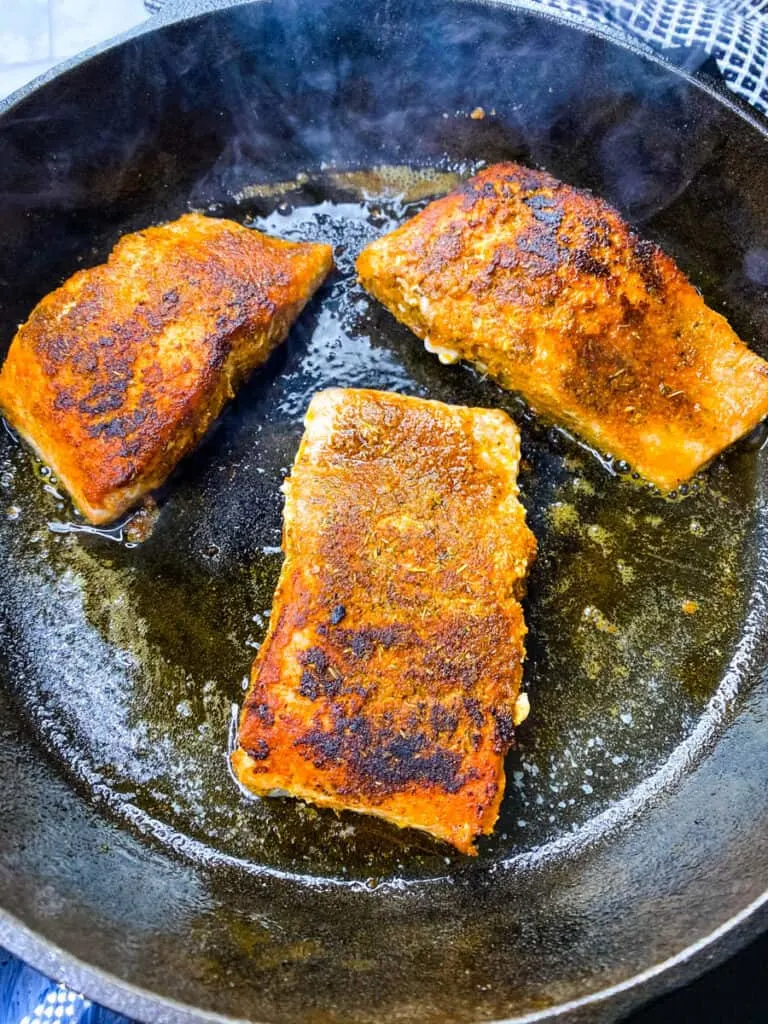 blackened salmon cooking in a cast iron skillet