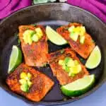 blackened salmon in a cast iron skillet topped with pineapple and avocado