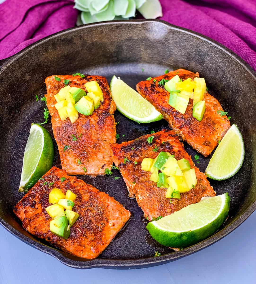 blackened salmon in a cast iron skillet topped with pineapple and avocado