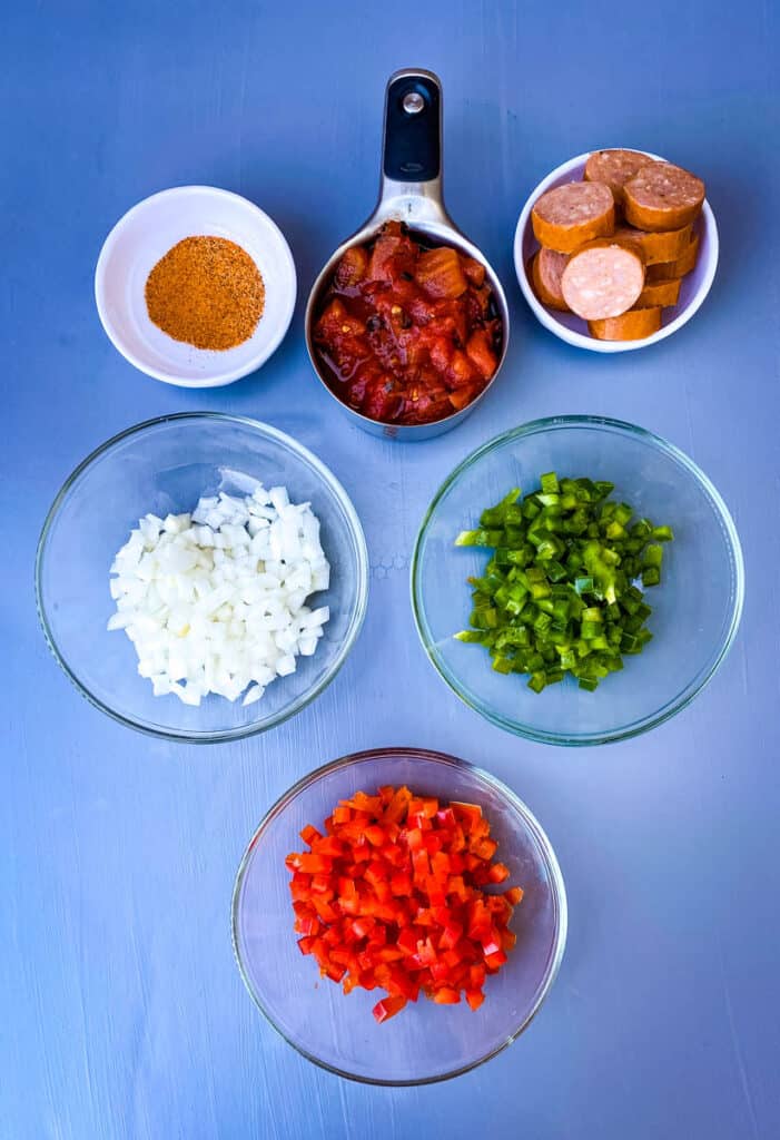 Cajun seasoning, chopped onions, chopped red and green peppers, sliced andouille sausage, and fire roasted tomatoes in separate bowls