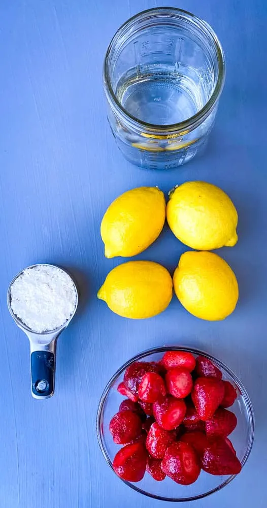 fresh lemons, fresh strawberries, water, and sweetener on a flat surface