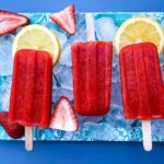 Zuckerfreie Erdbeer-Zitronen-Popsicles auf einer flachen Oberfläche mit Eis, Frische Zitronen und Erdbeeren