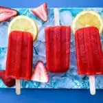 sugar free strawberry lemon popsicles on a flat surface with ice, fresh lemons and strawberries