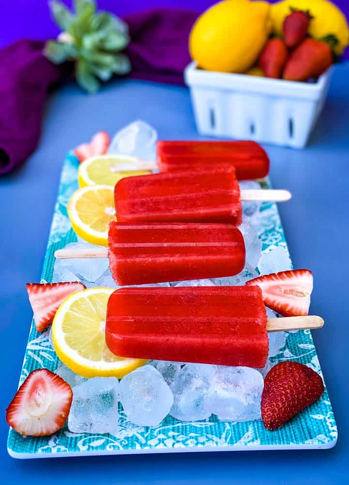 sugar free strawberry lemon popsicles on a flat surface with ice, fresh lemons and strawberries