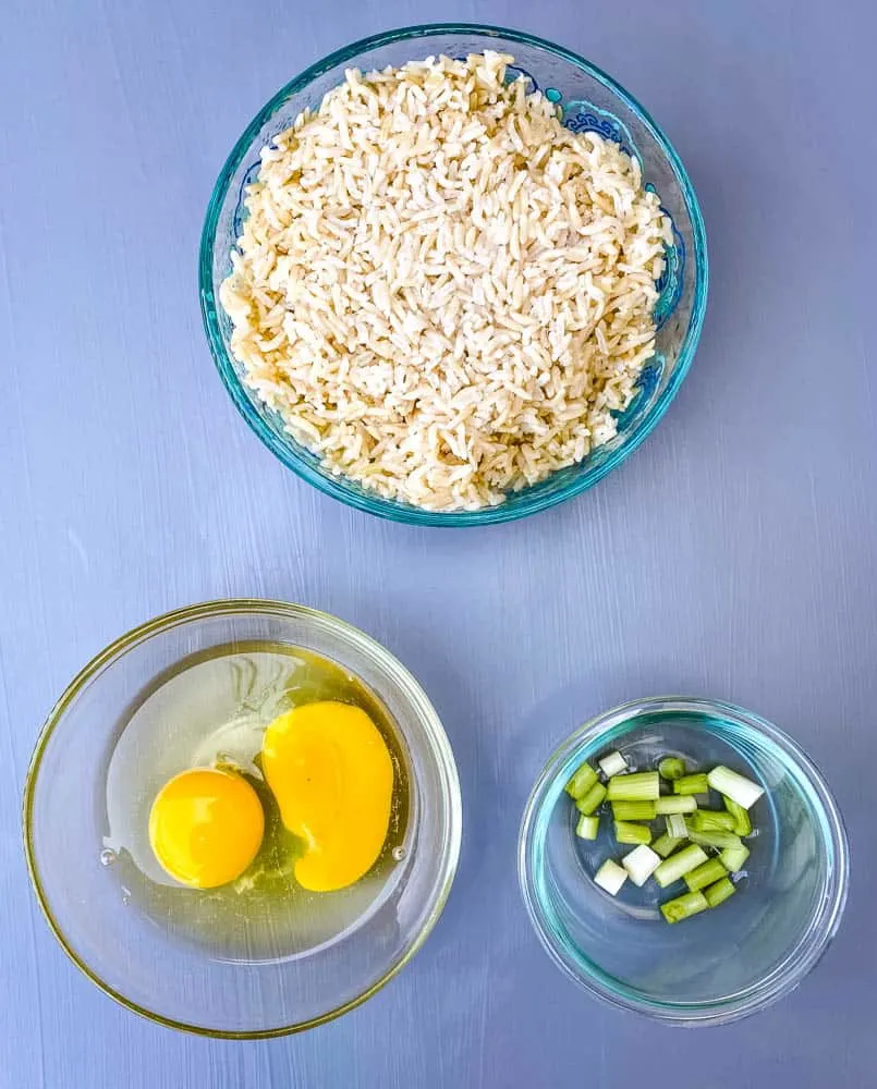 cooked and cold brown rice, raw eggs, and green onions in separate bowls