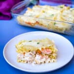 a slice of seafood lasagna on a plate with a baking pan of lasagna