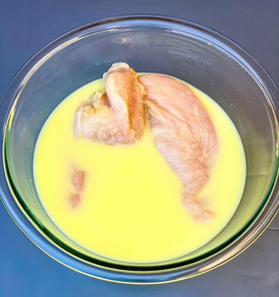 raw chicken breasts in a glass bowl with pickle juice and buttermilk