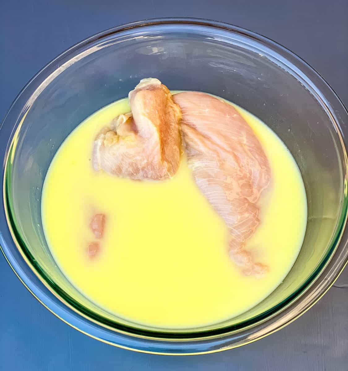 raw chicken breasts in a glass bowl with pickle juice and buttermilk