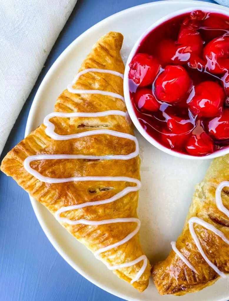 air fryer turnovers on a white plate with a bowl of cherries