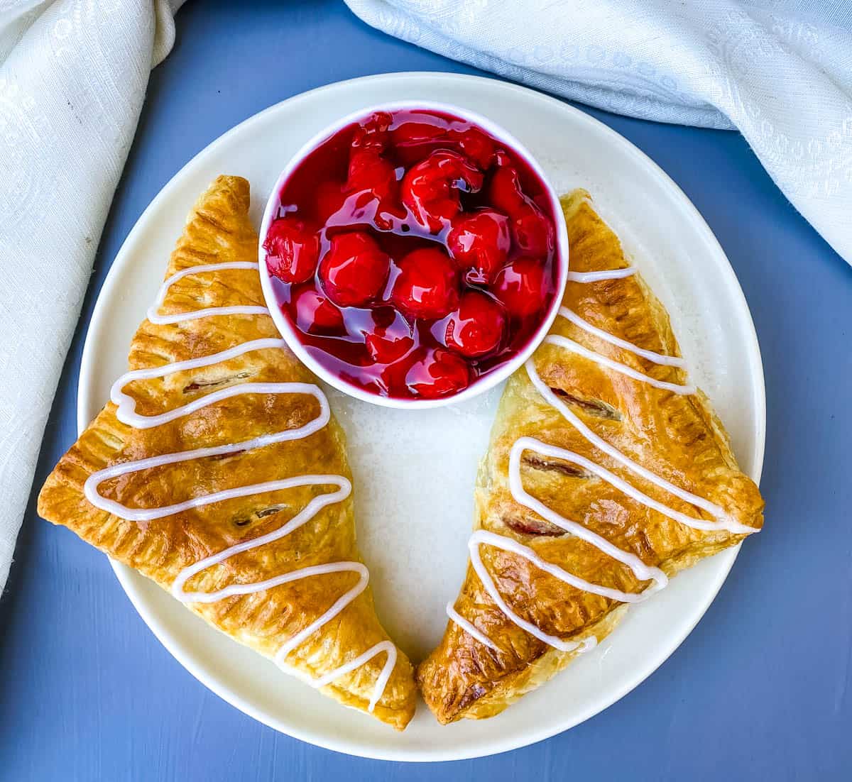 air fryer turnovers on a white plate with a bowl of cherries