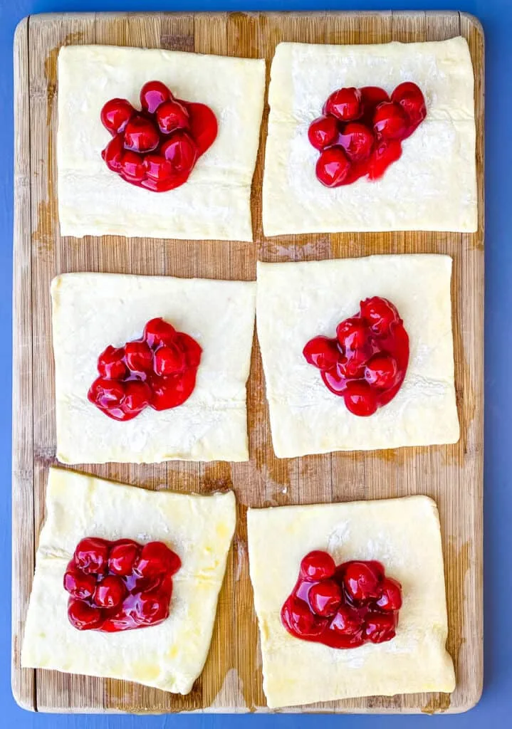 puff pastry filled with cherry pie filling on a bamboo cutting board