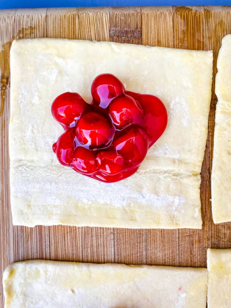 puff pastry filled with cherry pie filling on a bamboo cutting board