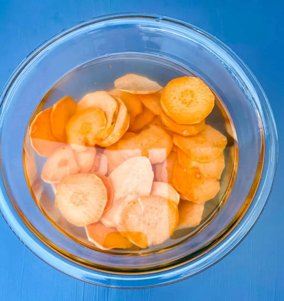 raw sliced sweet potato chips in a glass bowl with water