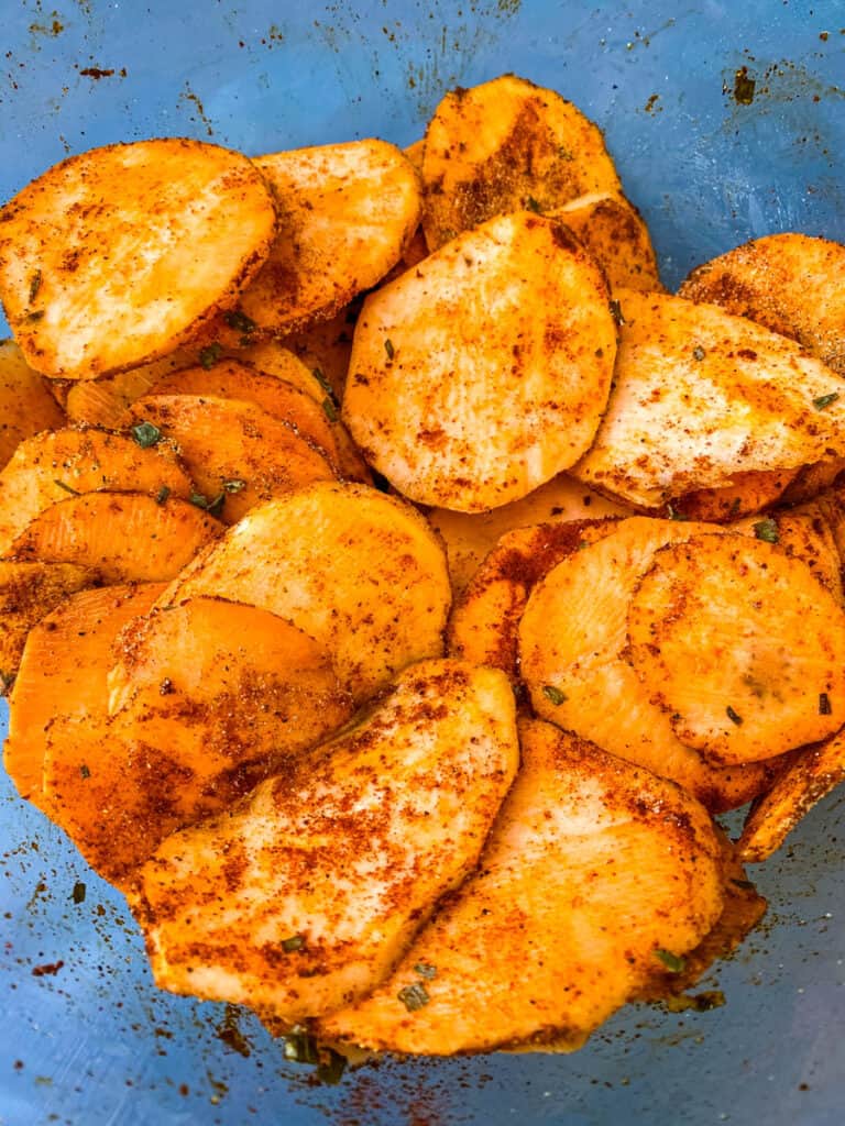 raw sliced sweet potato chips in a glass bowl sprinkled with seasonings