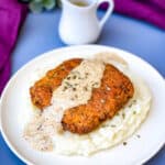 keto low carb chicken fried steak with country gravy on a bed of cauliflower mash on a white plate