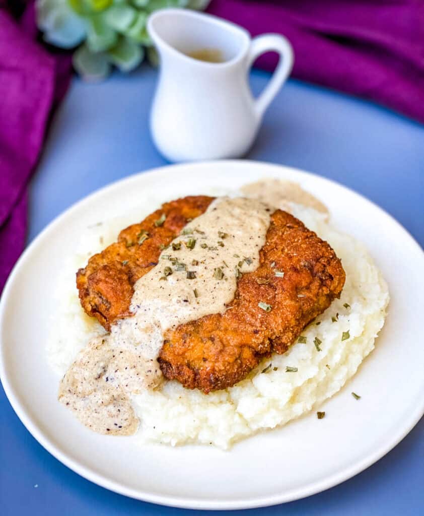keto low carb chicken fried steak with country gravy on a bed of cauliflower mash on a white plate