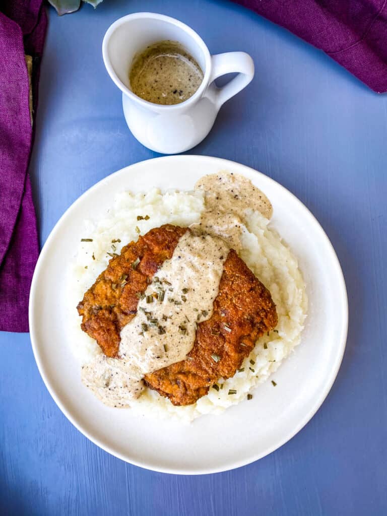 keto low carb chicken fried steak with country gravy on a bed of cauliflower mash on a white plate