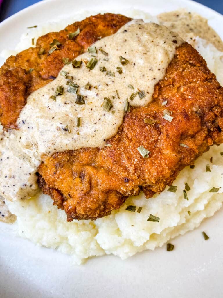 keto low carb chicken fried steak with country gravy on a bed of cauliflower mash on a white plate