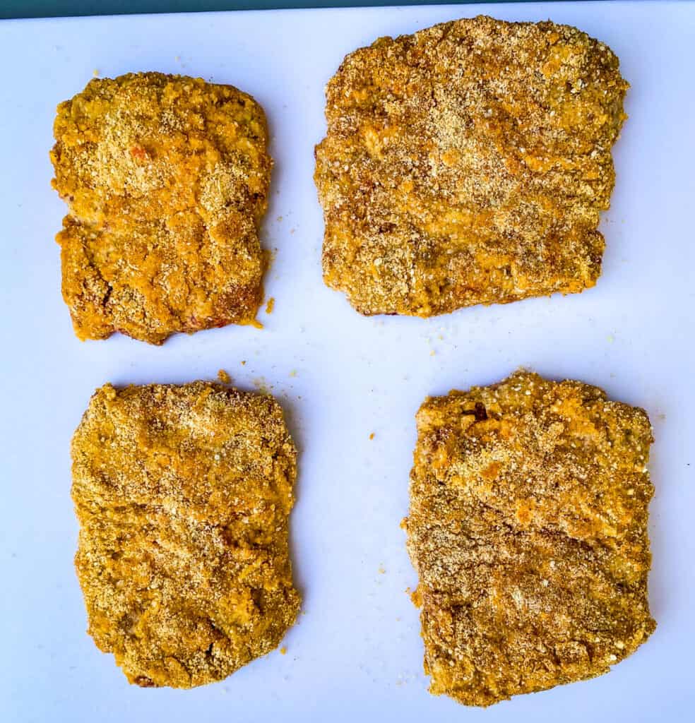 raw and bread keto chicken fried steaks on a white cutting board