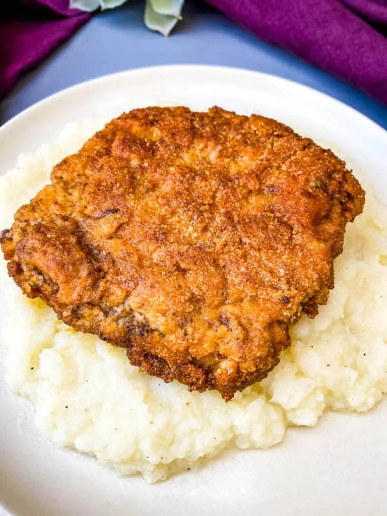 keto low carb chicken fried steak on a bed of cauliflower mash on a white plate