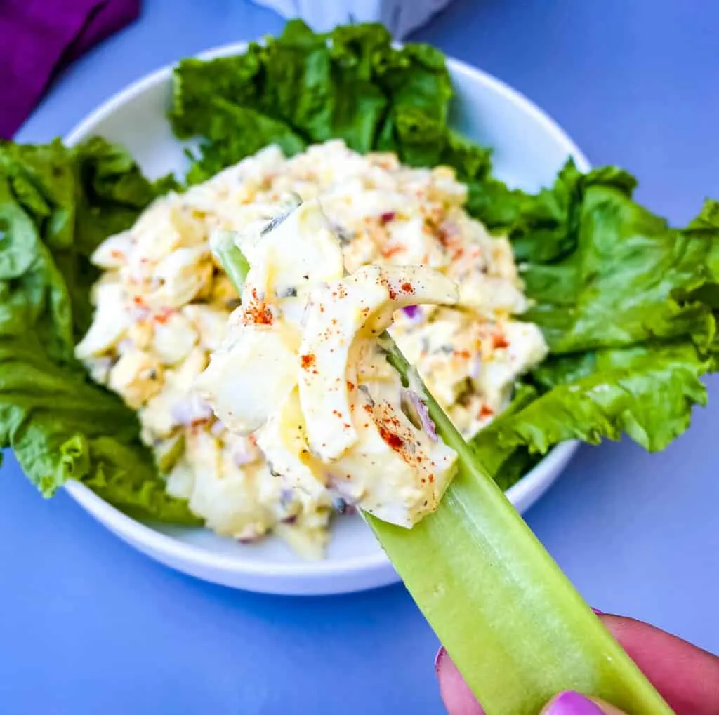 person holding a piece of celery with keto egg salad on the celery