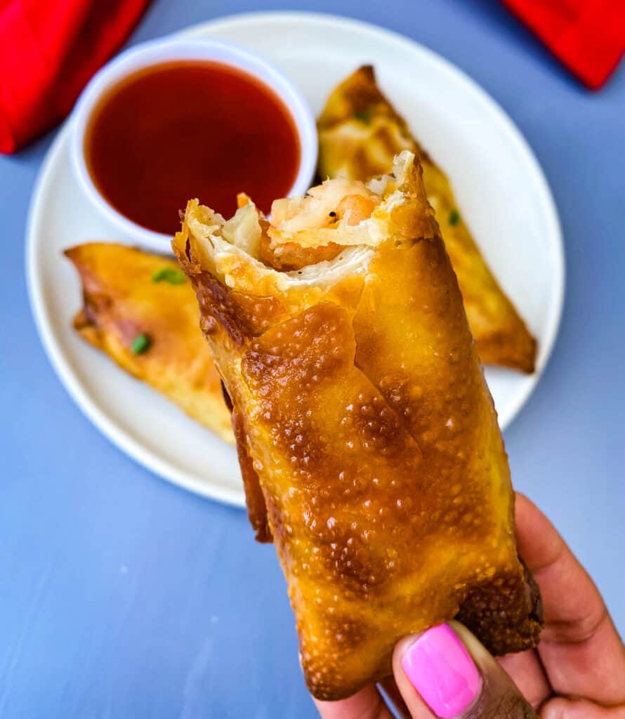 person holding shrimp egg roll with a bite taken out