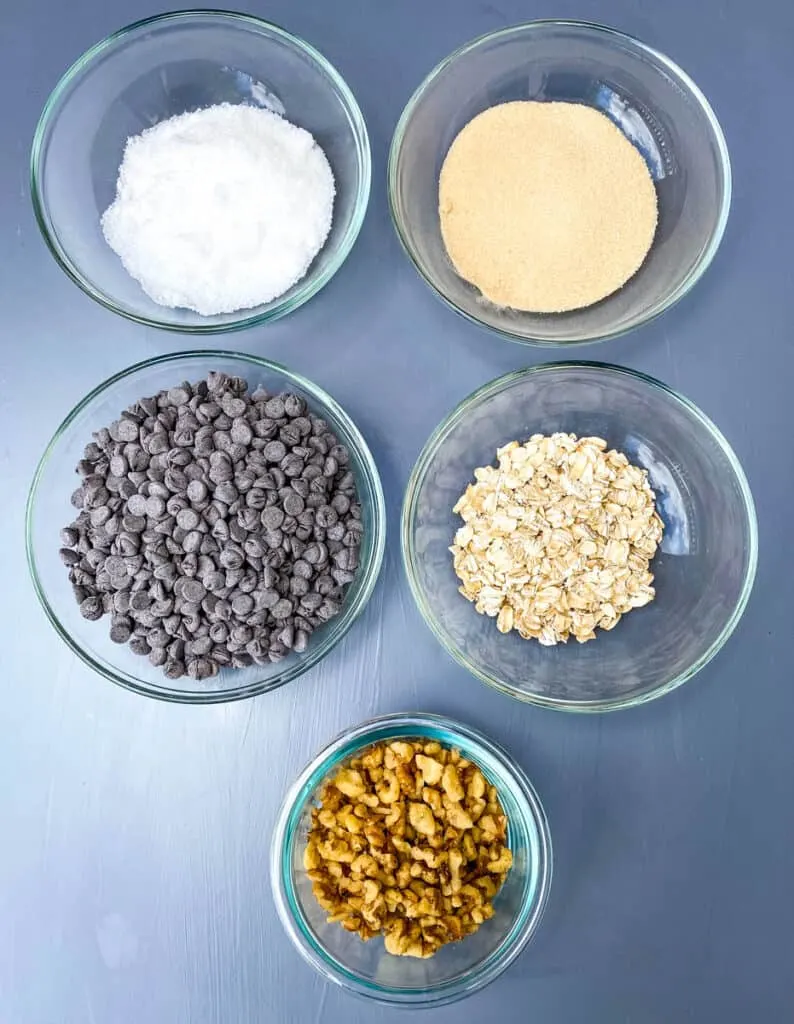 white sugar, brown sugar, chocolate chips, rolled oats, and walnuts in separate glass bowls