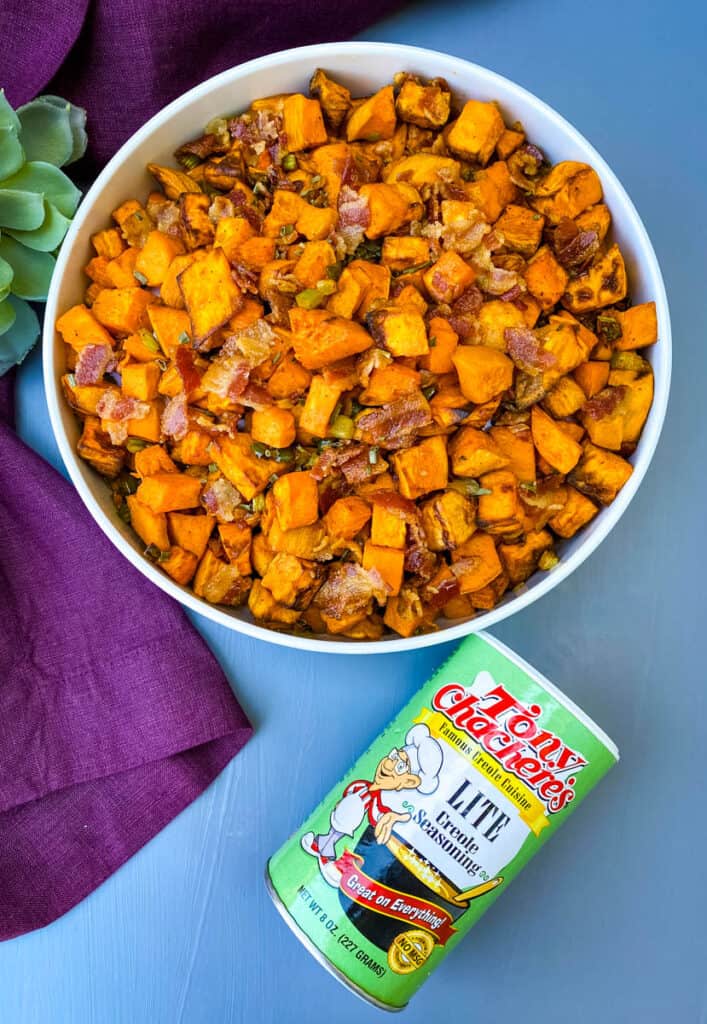 air fryer sweet potato hash with chopped bacon in a white bowl and a bottle of tony chachere's creole seasoning