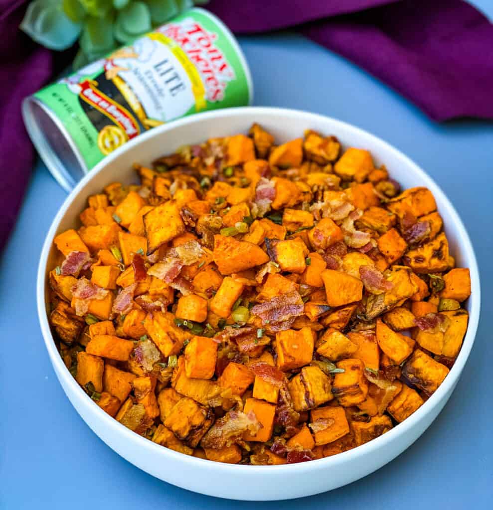 air fryer sweet potato hash with chopped bacon in a white bowl and a bottle of tony chachere's creole seasoning