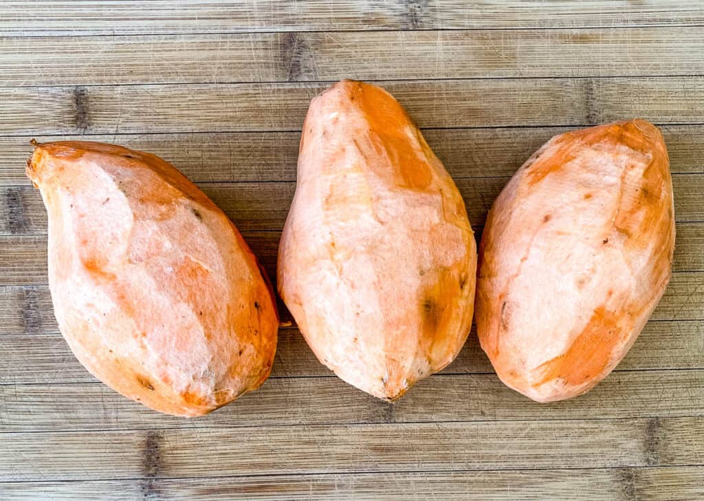 raw sweet potatoes on a bamboo cutting board