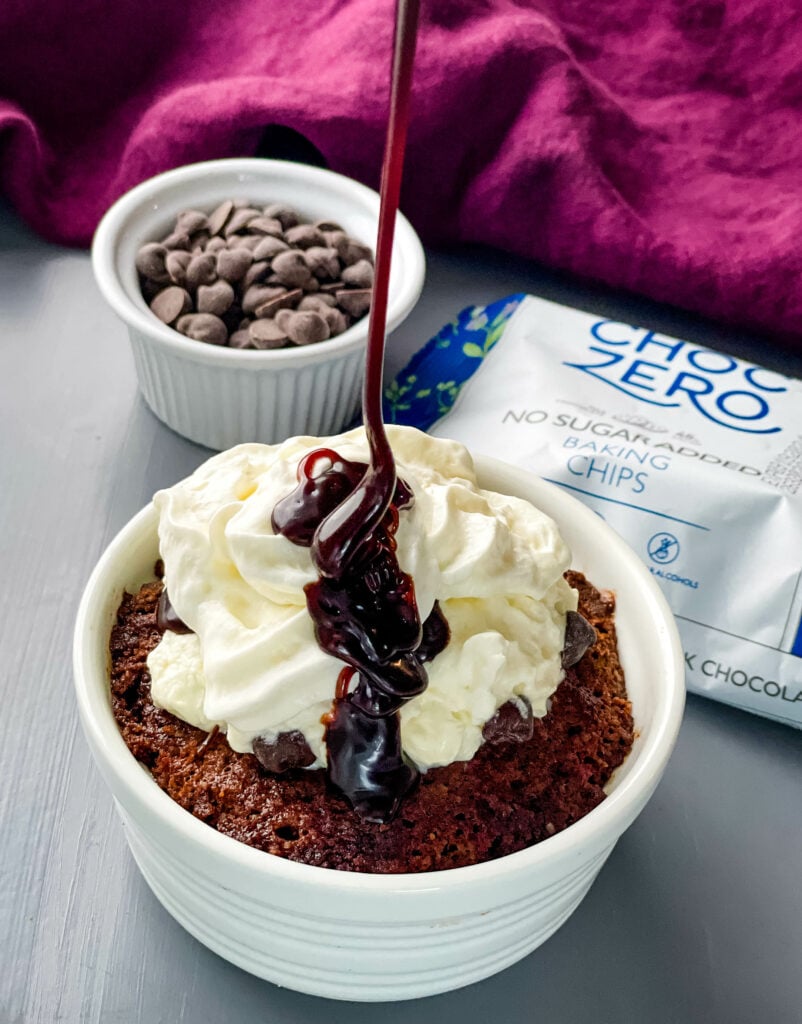 keto chocolate mug cake topped with whipped cream and drizzled with chocolate syrup