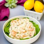 seafood crab salad with shrimp in a white bowl with spinach and a bowl of lemons