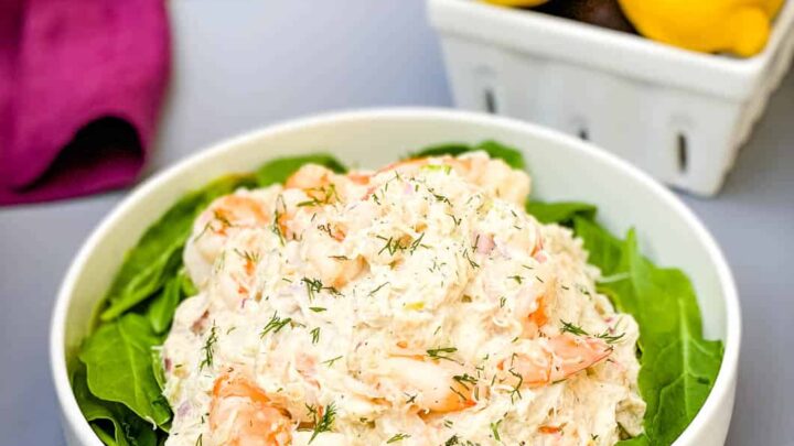 seafood crab salad with shrimp in a white bowl with spinach and a bowl of lemons