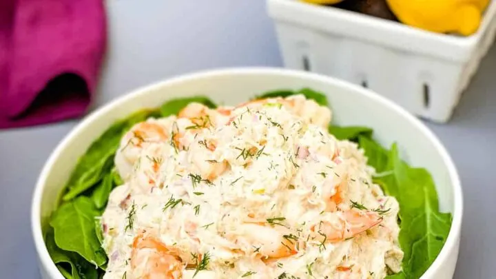 seafood crab salad with shrimp in a white bowl with spinach and a bowl of lemons