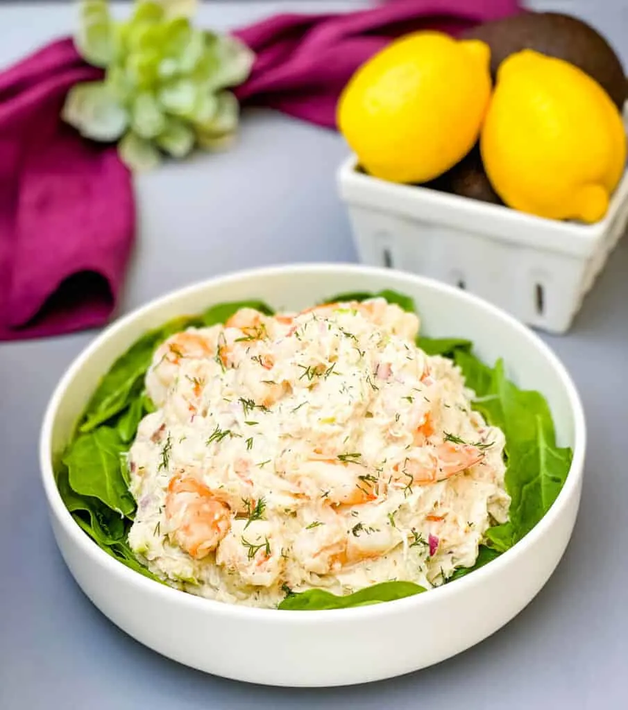 seafood crab salad with shrimp in a white bowl with spinach and a bowl of lemons