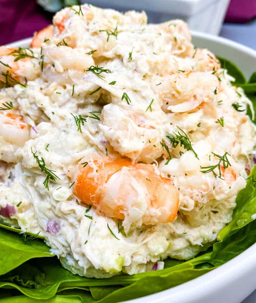 seafood crab salad with shrimp in a white bowl with spinach and a bowl of lemons