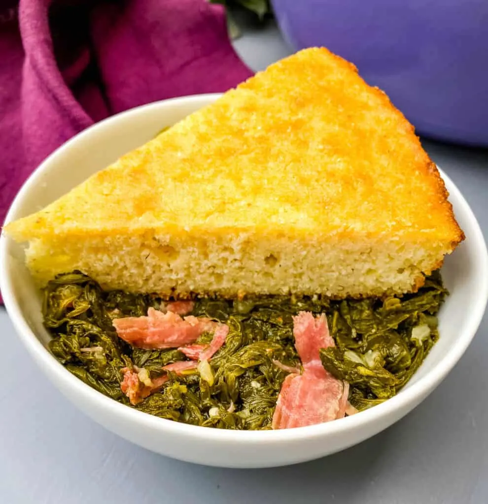 a bowl of southern mustard greens with smoked turkey and a slice of cornbread