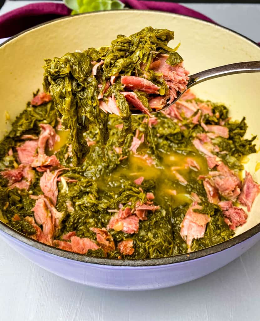 a spoonful of mustard greens held over a Dutch oven