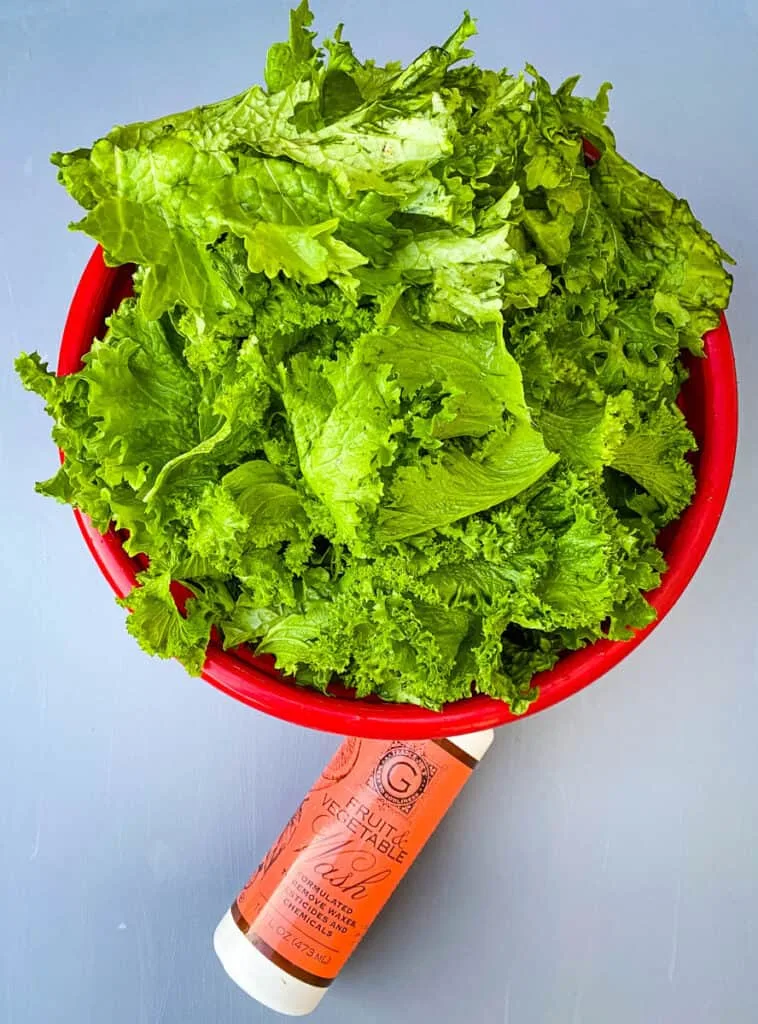 raw and fresh mustard greens in a red bowl with a bottle of produce cleaner