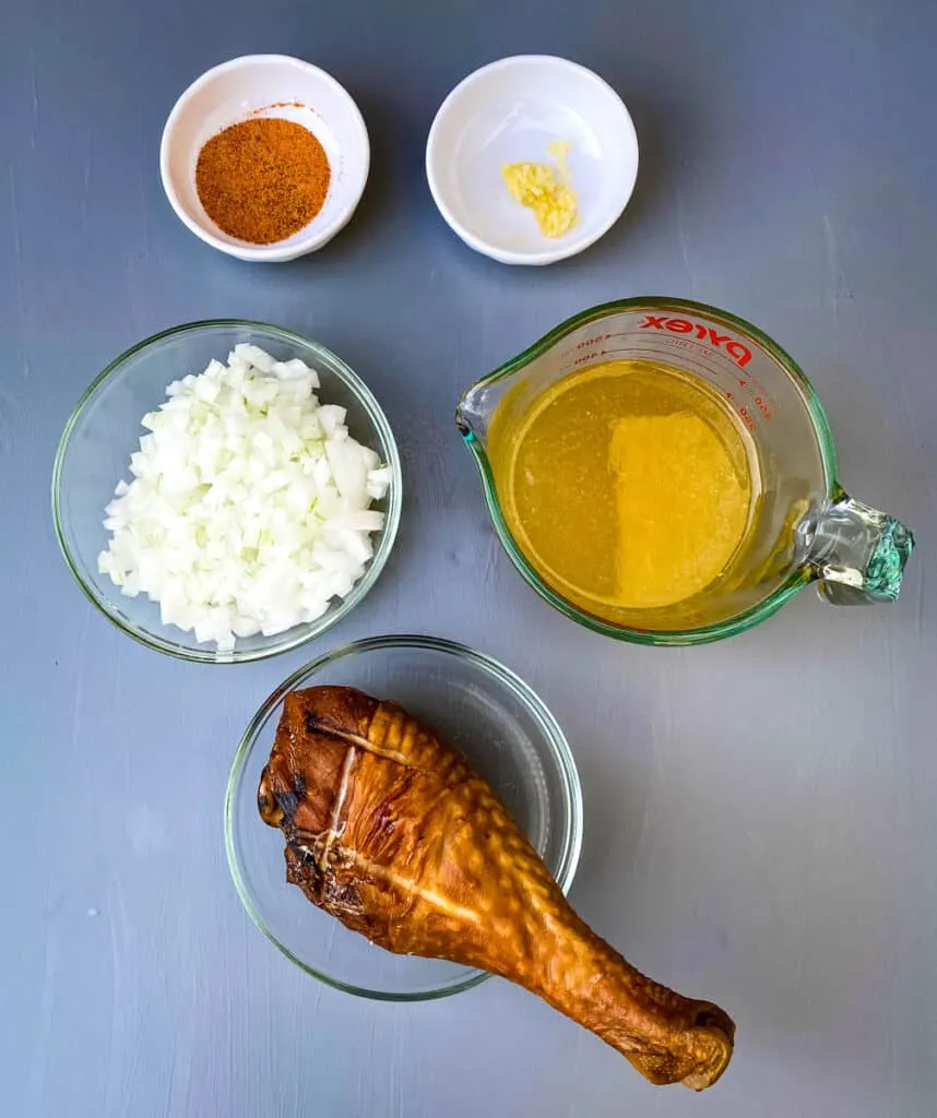 Creole seasoning, garlic, chopped onions, chicken broth, and smoked turkey on a flat surface