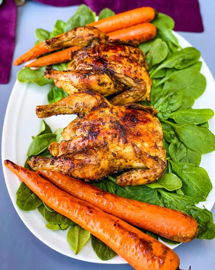 air fryer Cornish hens, fresh spinach, and carrots on a white plate